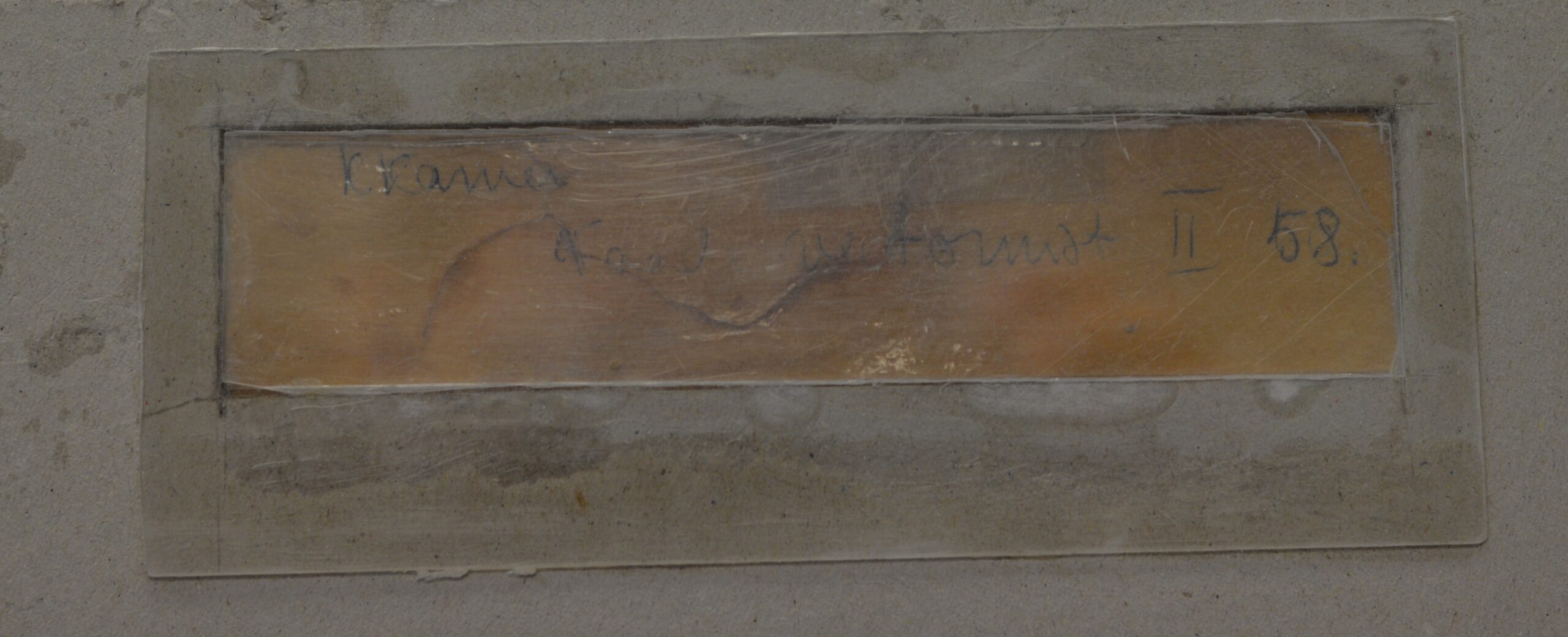 Rectangular wooden plaque embedded in a dusty concrete floor, with faded handwritten text and a wavy line across it.